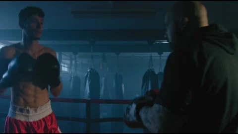 Boxer training with trainer in ring in dark room Stock Footage 275089400