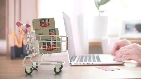 Boxes with RITE AID logo in shopping trolley near laptop. Editorial online store Stock Illustration