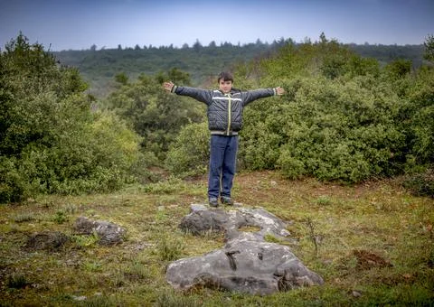 Boy 10 years old standing on a big rock and waving his hands Stock Photos