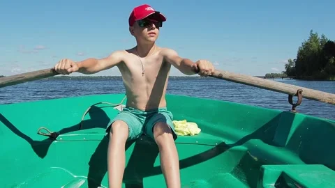 The boy is 12 years old rowing the oars, sailing the boat on the river. Video stock 233578209