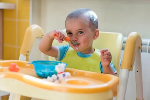 The boy 2 years eats porridge. Children's table. The concept of the child's i Stock Photos