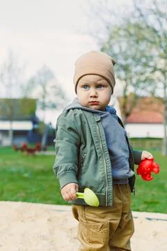 A boy of 2 years old in a spring jacket and hat plays with sand in a sandbo.. Stock-Fotos