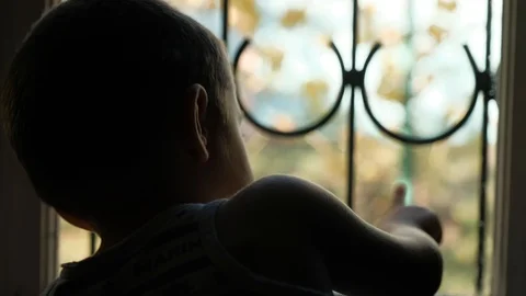 The boy is 3-5 years old outside the window with a lattice Stock Footage 98416947