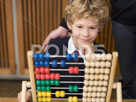 Boy (4-7) sitting by abacus, hand on chin, smiling Stock Photos