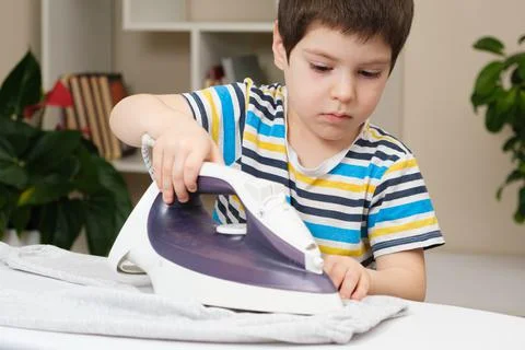A boy of 4 years learns to hold an iron, iron clothes on an ironing board. He 写真素材