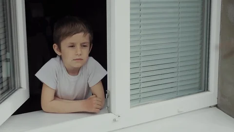 A boy of 5 years old is alone at the window with shutters. Stock Footage 127960286