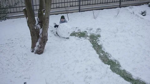 Boy 5 years old gray overalls makes snowman from snow backyard high angle view Stock-Footage 260653028