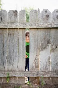 Boy (6-7) looking through hole in fence Foto stock