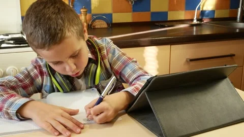 A boy of 6-7 years old looks at the tablet screen, listens to the teacher and Stock Footage 230899890