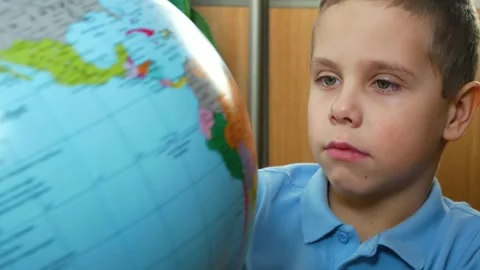 A boy of 6-7 years old examines a globe. Teaching children at school. Children Stock Footage 267186197