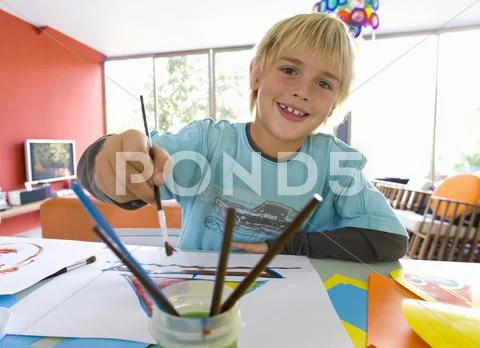 Boy (6-8) painting at table, smiling, portrait Stock Photos