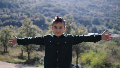 Boy 8 years old stands scouting his hands amid mountains in sunny weather Stock Footage 127769179
