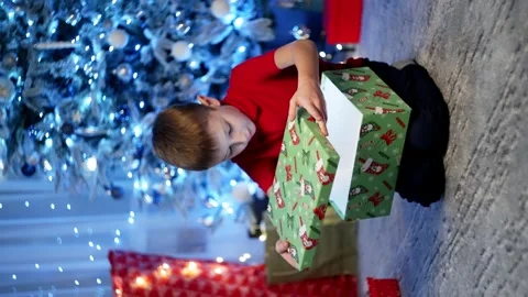 The boy is amazed to open presents in a room where the Christmas tree Stock Footage 259084796