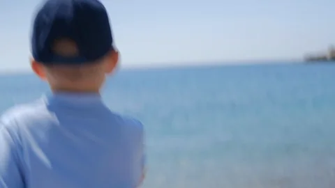Boy and dad throws a pebble at sea. Family  sitting with back forward at beach Stock Footage 107021260