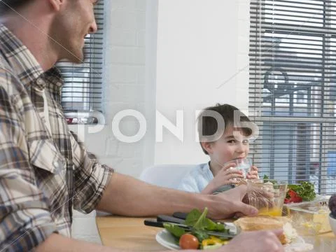 Boy And Father Having Meal At Dining Table Stock Photos
