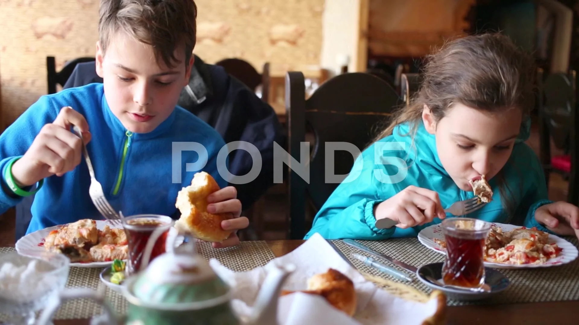 Boy and girl eat meat with vegetables sitting at table in cafe.