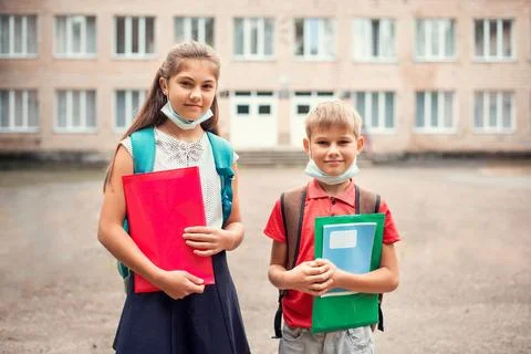 Boy and girl with school bags wearing medical masks near school Stock Photos