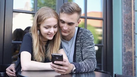 Boy and girl watch something on the phone sitting in a cafe Stock Footage
