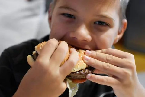 Boy with appetite eats delicious hamburger. child bites off large piece of sa Stock Photos