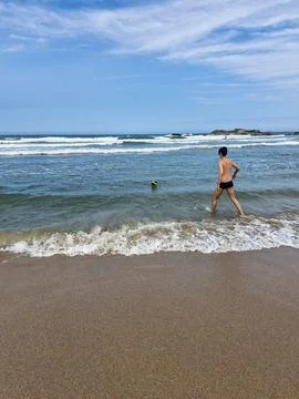 Boy approaching the ocean waves to catch the ball Stock Photos