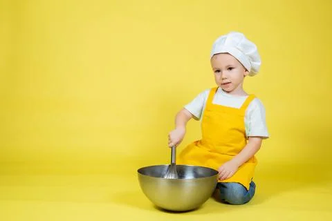 Boy in apron and chef's hat sitting on the floor with a bowl and whisk Stock Photos