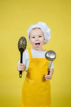 Boy in apron and chef's hat holds a ladle and slotted spoon Stock Photos