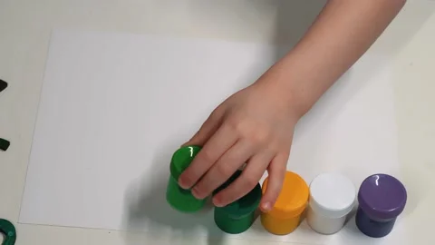 The boy arranges cans of paint on a sheet of paper before drawing. The child Stock Footage 230669234