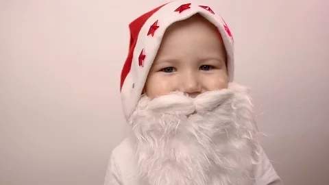 Boy with artificial beard in Santa Claus hat smiles, laughs, raises thumbs up Stock Footage 119233623