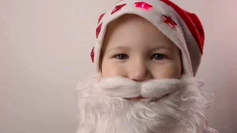 Boy with artificial beard in Santa Claus hat smiles, laughs, raises thumbs up Stock Footage 119387747