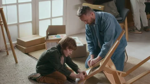Boy Assembling Chair with his Father, Surrounded by Boxes After Relocation Video stock 318081193