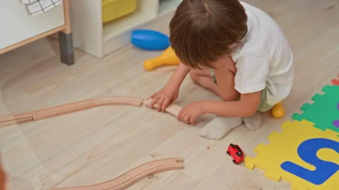 Boy assembling wooden train track with hands while sitting on floor in buil.. Stock Footage 337385788