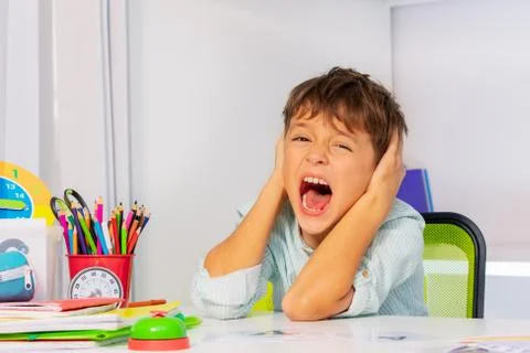 Boy with autism at the table close ears and scream Stock Photos