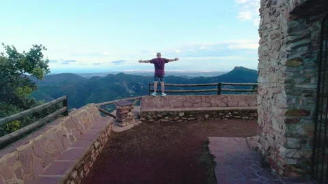 Boy from back next to cliff raises his arms to fly and drone flies over his head Stock Footage 138895550