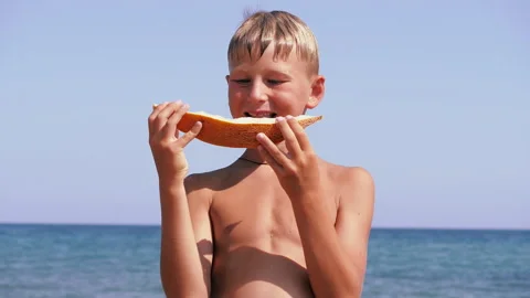 Boy on the background of the sea bites off a piece of juicy melon. Stock Footage 223931692