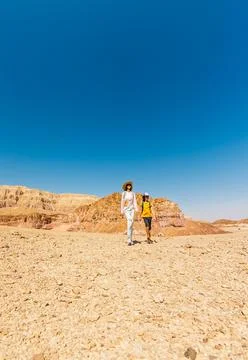 A boy with a backpack and a map walks next to his mother through the desert.. Stock Photos