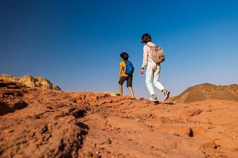 A boy with a backpack and a map walks next to his mother through the desert.. Stock Photos