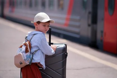 Boy with backpack and suitcase waiting for train on railway station platform. Stock Photos