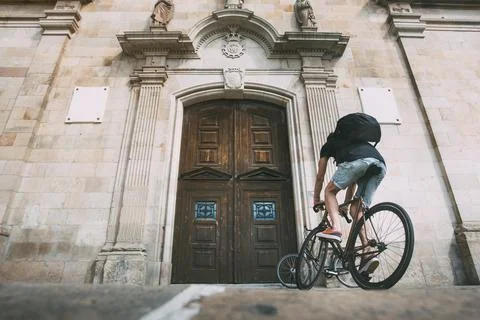 Boy with a backpack on a bike in front of a wooden door of a church . Backgro Stock Photos