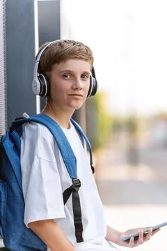 Boy with backpack looking at camera while using mobile phone and headphones 스톡 사진