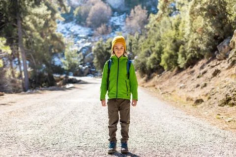A boy with a backpack in the middle of a forest road, a child is exploring wi Stock Photos