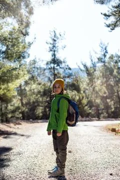 A boy with a backpack in the middle of a forest road, a child is exploring wi Stock Photos