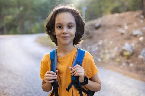 Boy with a backpack walks along a forest road. children's hike in the forest  Stock Photos