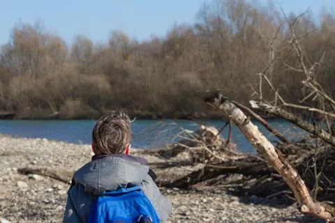 A boy with a backpack walks along a stone beach to a mountain river Stock Photos