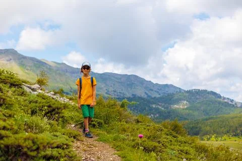 Boy with a backpack walks through a mountain meadow during the summer holiday Stock Photos