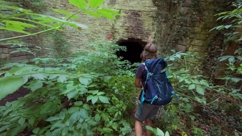 Boy with a backpack walks toward an abandoned stone tunnel and enters inside, ex Stock-Footage 326047327