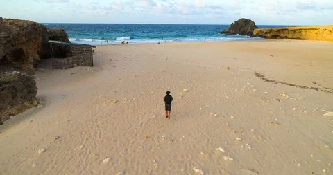A boy with a bag pack walks on a beach to a beautiful wild coast. Stock-Footage 97768061