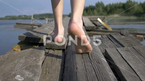 Boy bare feet walking along the old decrepit pier Stock Photos