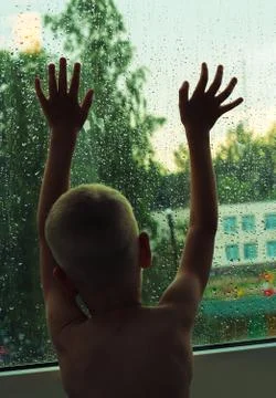 A boy with a bare torso stands by the window, rests his hands on the glass an Stock Photos