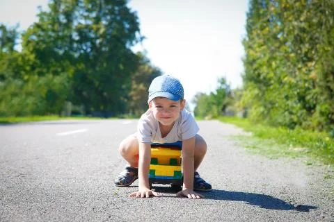 A boy in a baseball cap playing on an asphalt road with a large truck Stock Photos
