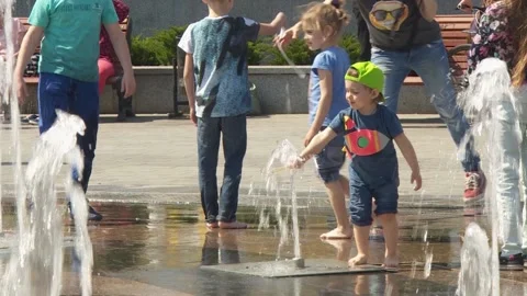 A boy in a baseball cap runs through the water jets of the fountain. bare feet Stock-Footage 139440468